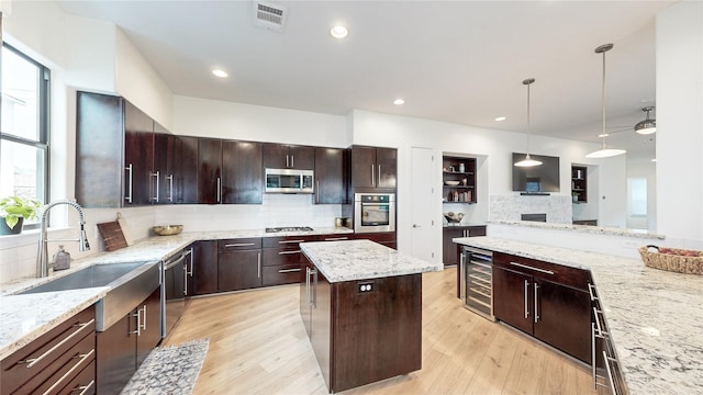 kitchen with appliances with stainless steel finishes, decorative light fixtures, wine cooler, a center island, and light stone countertops