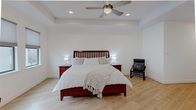 bedroom featuring ceiling fan, a tray ceiling, and light hardwood / wood-style flooring