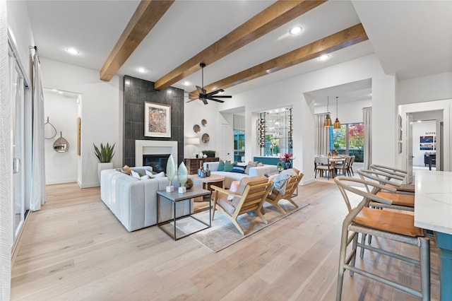 living room with beam ceiling, a fireplace, light hardwood / wood-style floors, and ceiling fan