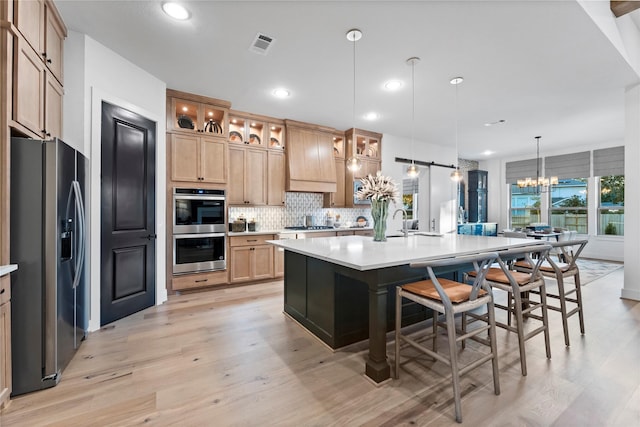 kitchen with appliances with stainless steel finishes, decorative light fixtures, tasteful backsplash, a kitchen bar, and a large island with sink