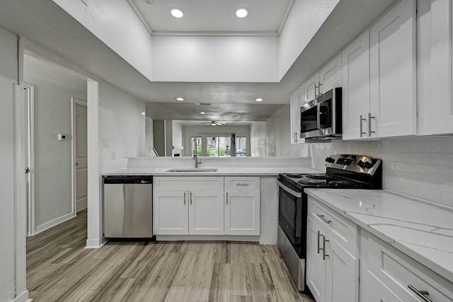 kitchen with decorative backsplash, white cabinets, appliances with stainless steel finishes, light wood-type flooring, and a sink