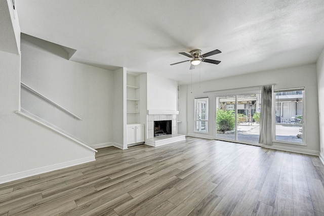 unfurnished living room with built in shelves, ceiling fan, a fireplace, and light hardwood / wood-style flooring