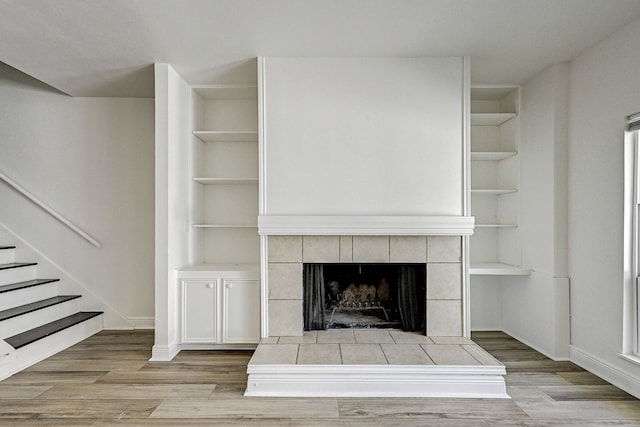 unfurnished living room with built in shelves, a tiled fireplace, and light wood-type flooring