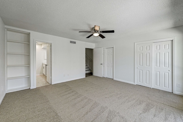 unfurnished bedroom with a textured ceiling, ceiling fan, carpet floors, visible vents, and two closets