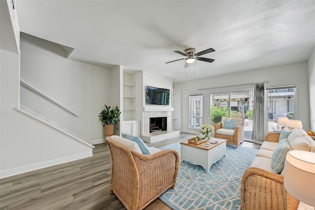 living room with a fireplace, wood finished floors, a ceiling fan, built in features, and baseboards