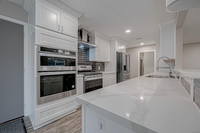 kitchen featuring appliances with stainless steel finishes, sink, wall chimney range hood, and white cabinets