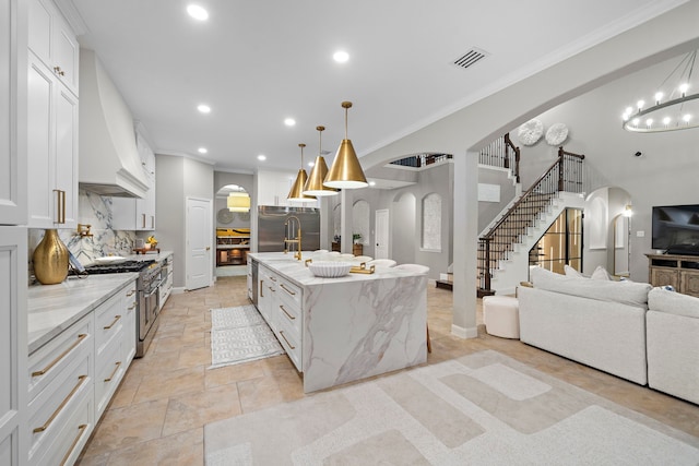 kitchen with pendant lighting, premium appliances, white cabinets, and a center island with sink