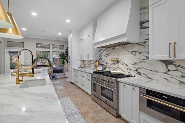 kitchen with premium range hood, appliances with stainless steel finishes, white cabinetry, sink, and light stone countertops