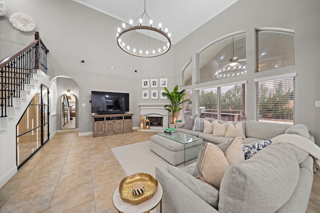 tiled living room featuring crown molding, a towering ceiling, and ceiling fan with notable chandelier