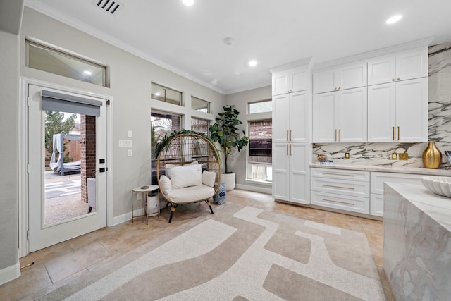 kitchen featuring white cabinetry, light stone countertops, decorative backsplash, and ornamental molding