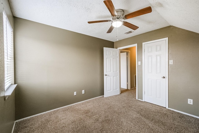 unfurnished bedroom with ceiling fan, lofted ceiling, carpet floors, and a textured ceiling