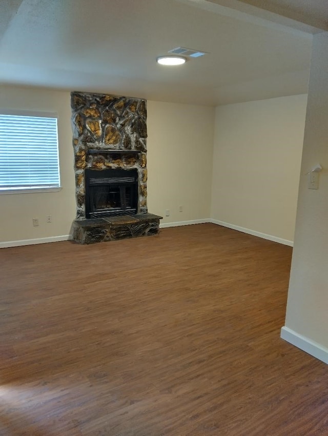 unfurnished living room with a stone fireplace and dark hardwood / wood-style floors