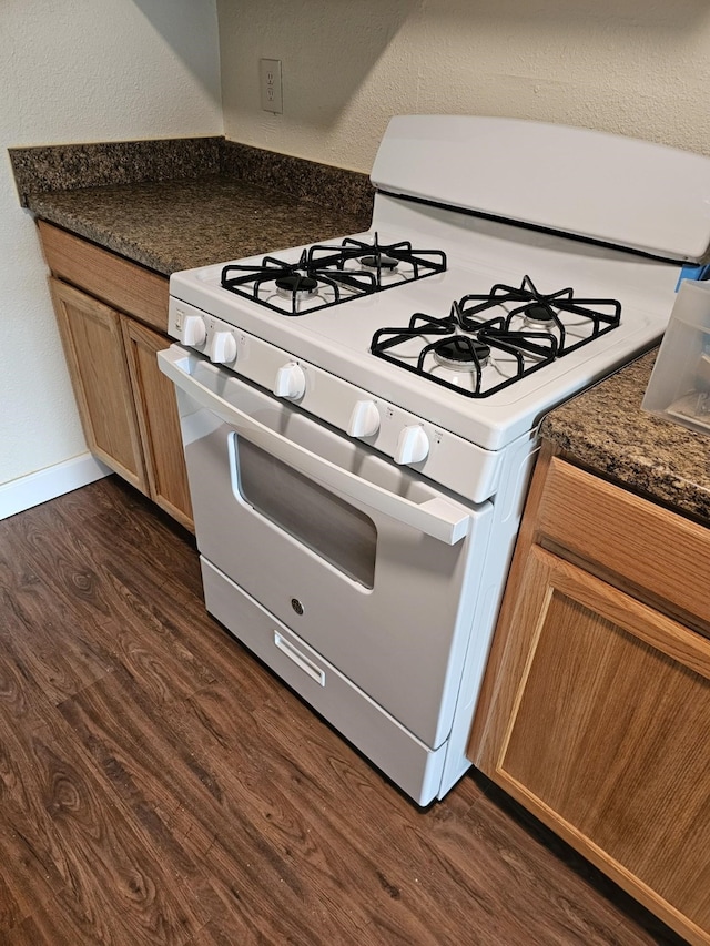 kitchen featuring dark hardwood / wood-style floors, white gas range, and dark stone countertops