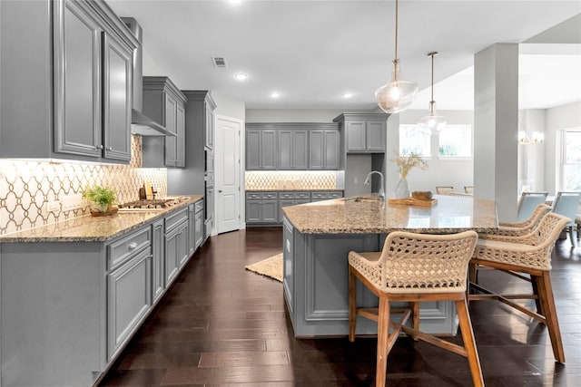 kitchen featuring gray cabinets, dark hardwood / wood-style floors, decorative light fixtures, decorative backsplash, and light stone counters