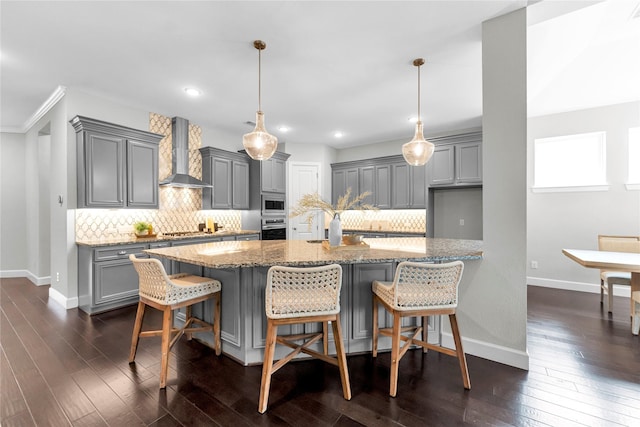 kitchen with light stone counters, stainless steel appliances, hanging light fixtures, and wall chimney range hood