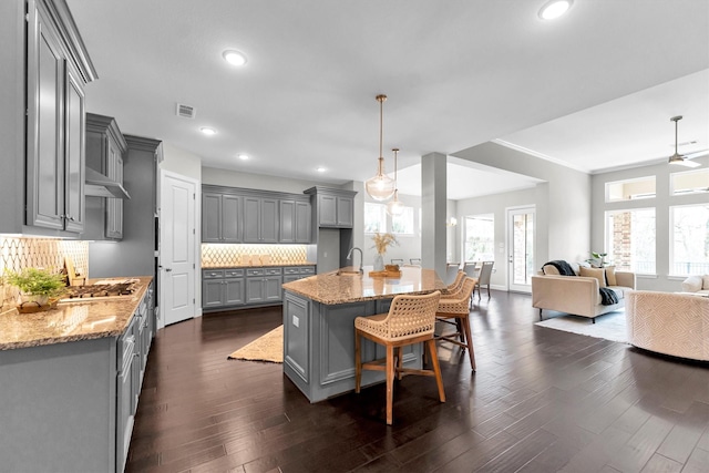 kitchen with pendant lighting, gray cabinets, light stone countertops, and backsplash