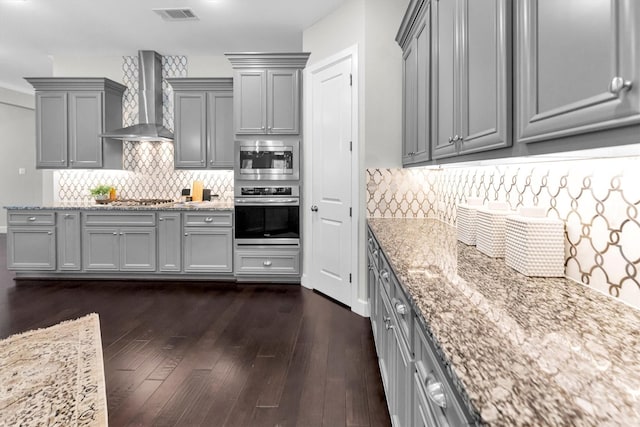 kitchen featuring stainless steel appliances, gray cabinetry, wall chimney range hood, and light stone counters