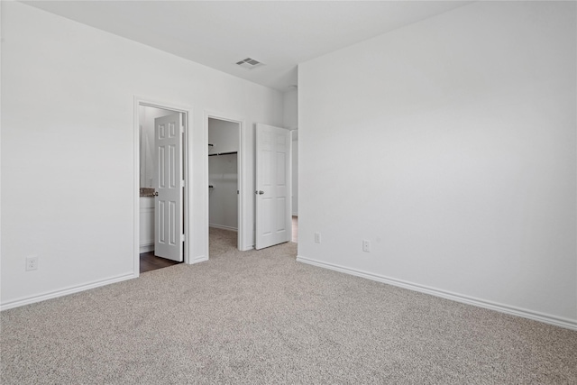 unfurnished bedroom featuring a walk in closet, ensuite bathroom, and carpet flooring