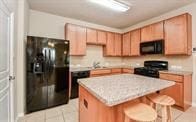 kitchen featuring light tile patterned flooring, a kitchen breakfast bar, a center island, and black appliances