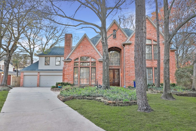 tudor home featuring concrete driveway, brick siding, a chimney, and a front yard