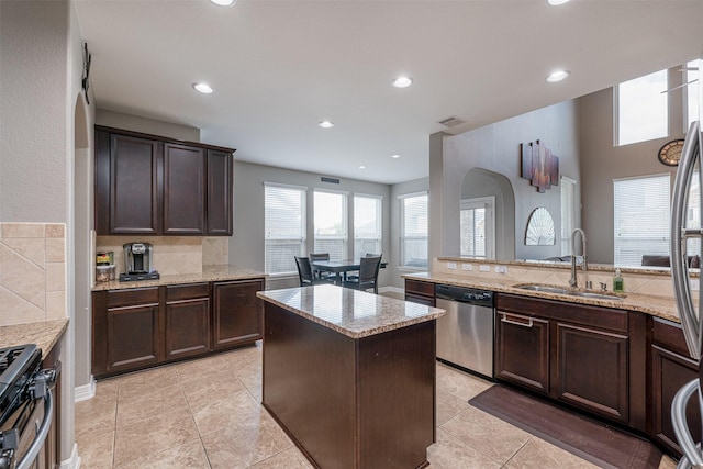 kitchen with gas stove, sink, light stone counters, a center island, and dishwasher