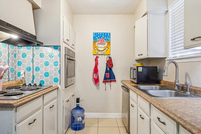 kitchen with sink, a textured ceiling, light tile patterned floors, appliances with stainless steel finishes, and white cabinets