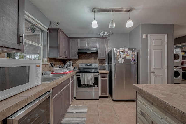 kitchen with pendant lighting, stainless steel appliances, stacked washer and clothes dryer, range hood, and beverage cooler