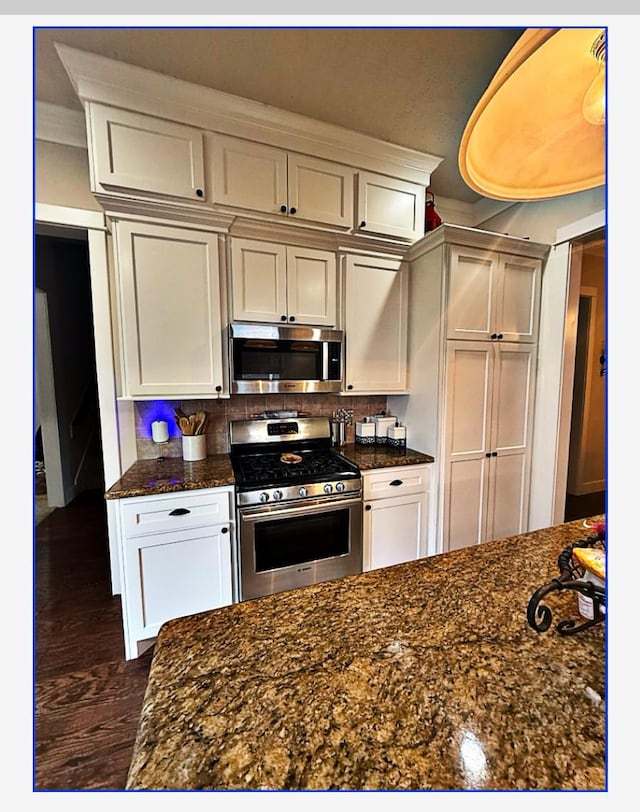 kitchen featuring tasteful backsplash, white cabinets, stainless steel appliances, and dark stone countertops