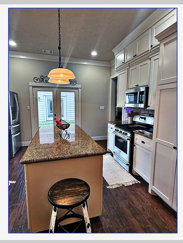 kitchen featuring appliances with stainless steel finishes, hanging light fixtures, a center island, a kitchen bar, and dark stone counters