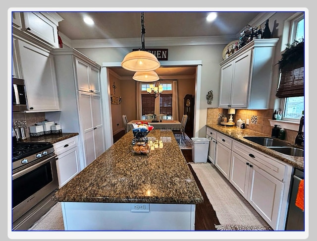 kitchen with sink, appliances with stainless steel finishes, backsplash, a kitchen island, and decorative light fixtures