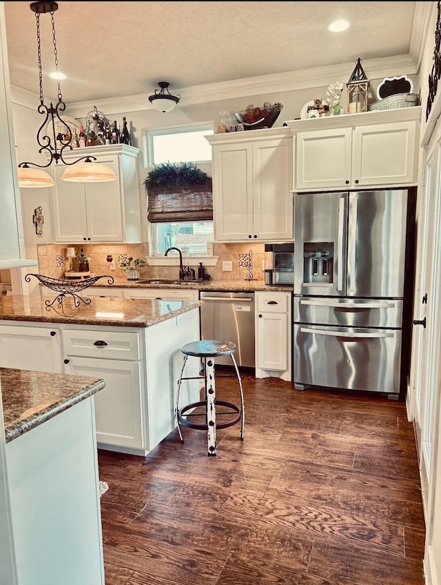 kitchen with white cabinets, a sink, stone counters, crown molding, and appliances with stainless steel finishes