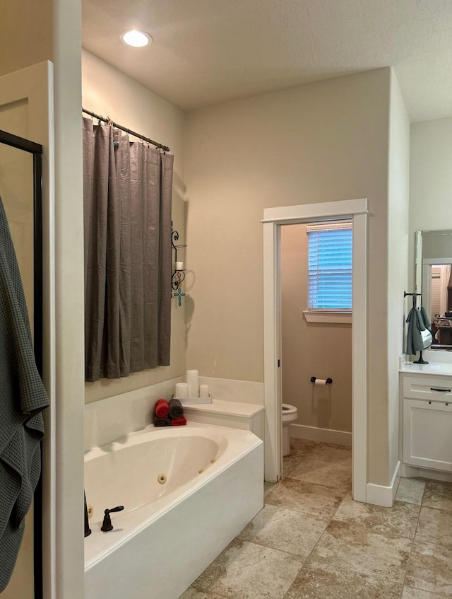 bathroom with toilet, vanity, a whirlpool tub, and baseboards