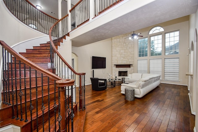 living room with hardwood / wood-style floors, a stone fireplace, ceiling fan, and a high ceiling