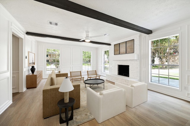 living room with a fireplace, beamed ceiling, a textured ceiling, and light wood-type flooring