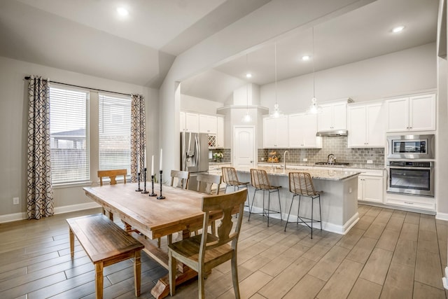 dining area with high vaulted ceiling, sink, and light hardwood / wood-style floors