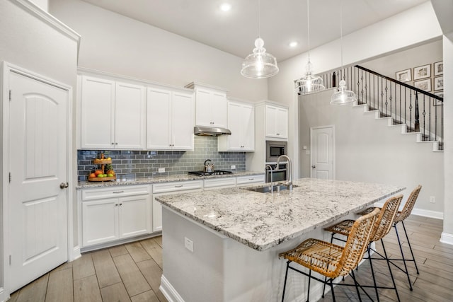 kitchen with a center island with sink, stainless steel appliances, hanging light fixtures, and white cabinets