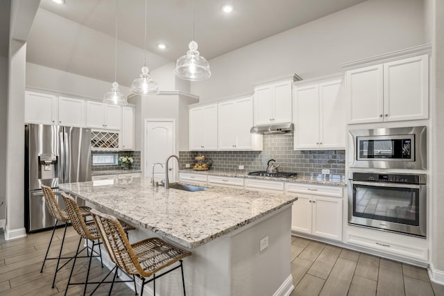 kitchen with an island with sink, appliances with stainless steel finishes, sink, and white cabinets