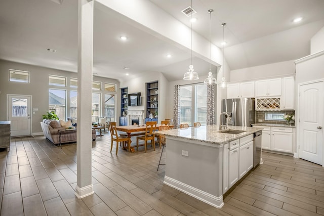 kitchen with appliances with stainless steel finishes, pendant lighting, white cabinetry, an island with sink, and sink