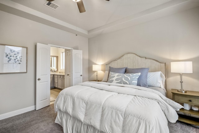 carpeted bedroom with a tray ceiling, ensuite bath, and ceiling fan