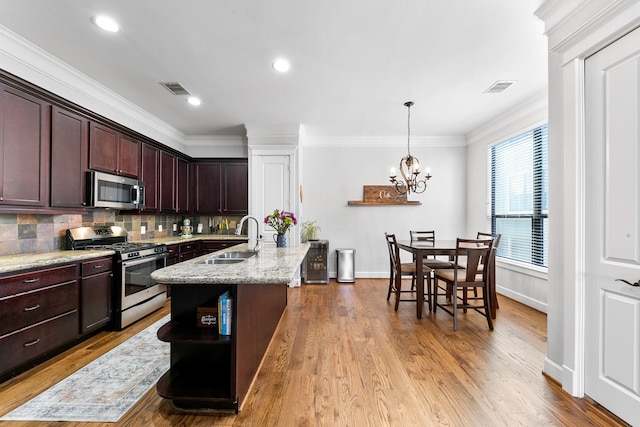 kitchen with decorative light fixtures, sink, stainless steel appliances, light stone countertops, and a center island with sink