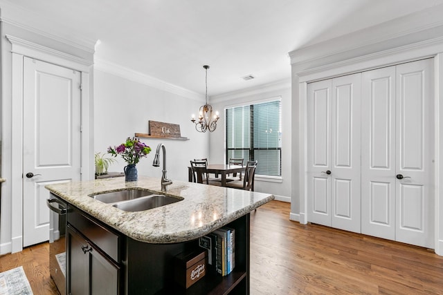 kitchen featuring sink, crown molding, pendant lighting, light stone countertops, and a kitchen island with sink