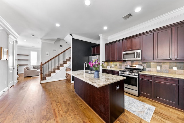 kitchen with stainless steel appliances, an island with sink, light wood-type flooring, and light stone counters