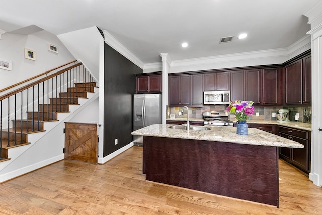 kitchen with sink, light stone counters, stainless steel appliances, a center island with sink, and light hardwood / wood-style flooring