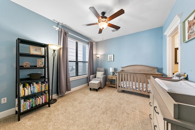 bedroom with a nursery area, light carpet, and ceiling fan