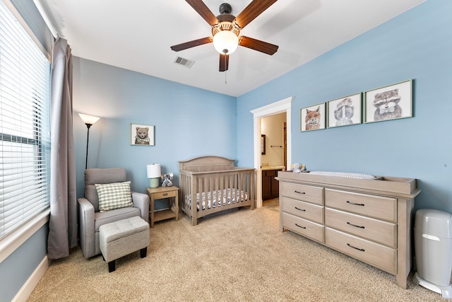 bedroom featuring a crib, light colored carpet, and ceiling fan