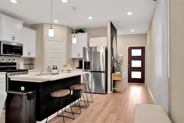 kitchen with white cabinetry, hanging light fixtures, light hardwood / wood-style floors, and appliances with stainless steel finishes