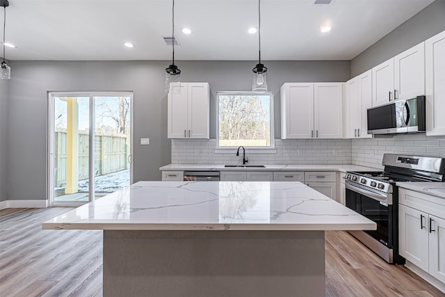 kitchen featuring appliances with stainless steel finishes, white cabinetry, a center island, light stone countertops, and decorative light fixtures