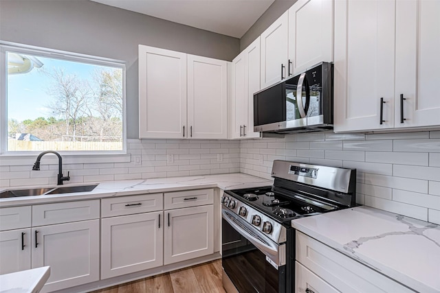 kitchen featuring white cabinetry, sink, decorative backsplash, light stone counters, and stainless steel appliances