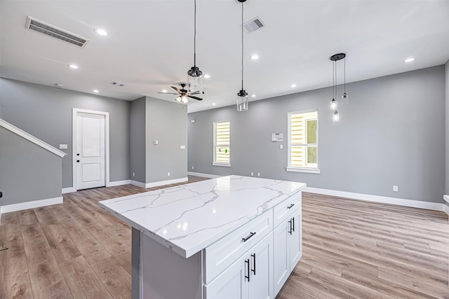 kitchen with light hardwood / wood-style flooring, white cabinetry, a center island, light stone counters, and decorative light fixtures