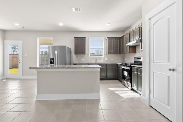 kitchen with appliances with stainless steel finishes, a center island, tasteful backsplash, light stone countertops, and light tile patterned flooring